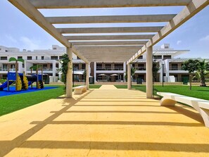 A covered walkway leading to a building with a playground and outdoor seating area. - Ground Floor Oasis at La Serena Golf (Los Alcazares)