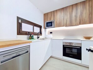 Een moderne keuken met witte kastjes, een ingebouwde magnetron, een vaatwasser en een kookplaat.