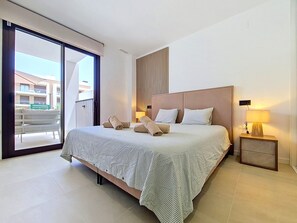 Une chambre d’hôtel moderne avec un grand lit, une table de chevet avec une lampe et une vue sur le balcon extérieur.