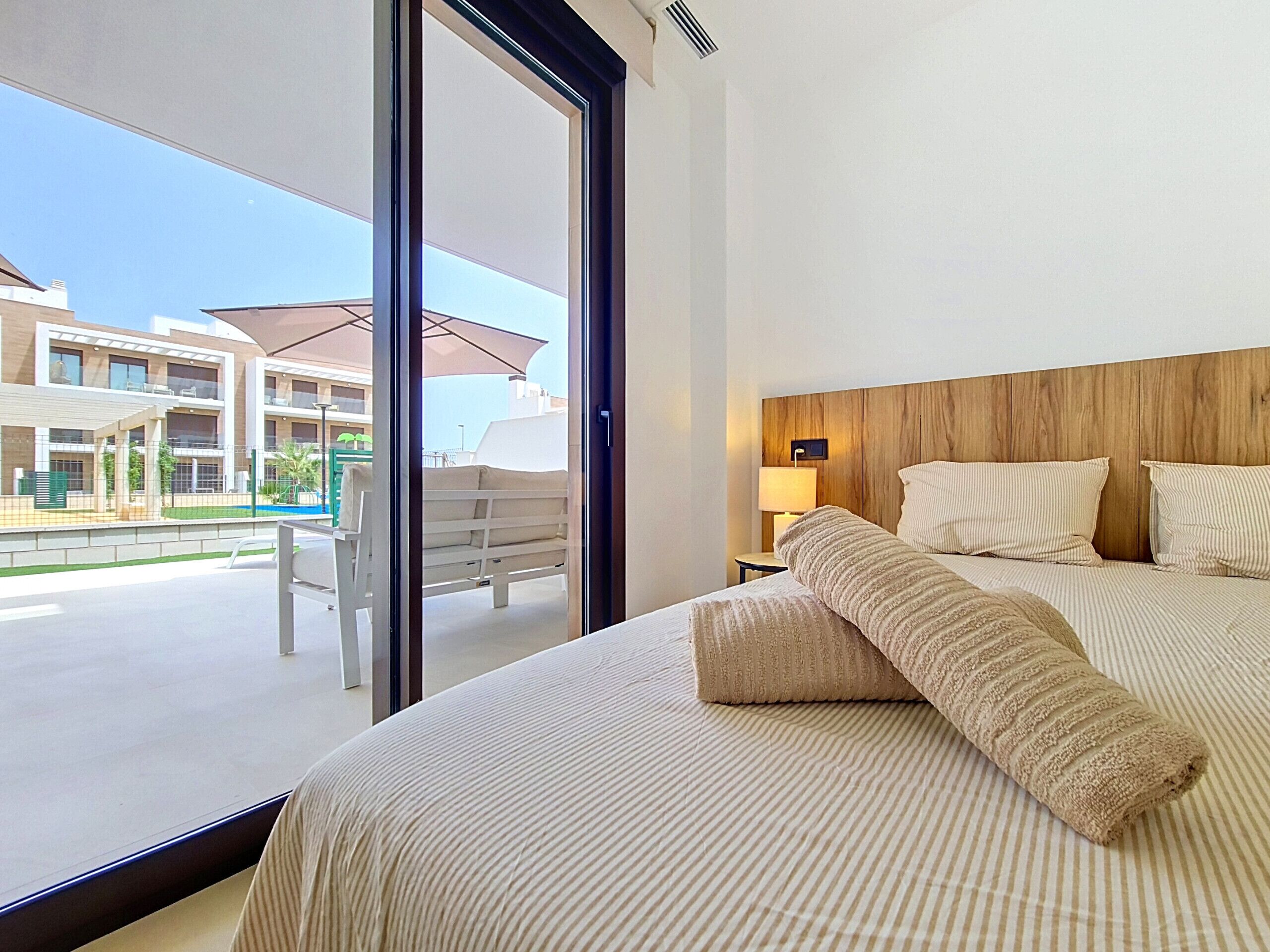 Une chambre d’hôtel avec un grand lit, une tête de lit en bois, une table de chevet et une vue sur l’espace extérieur.