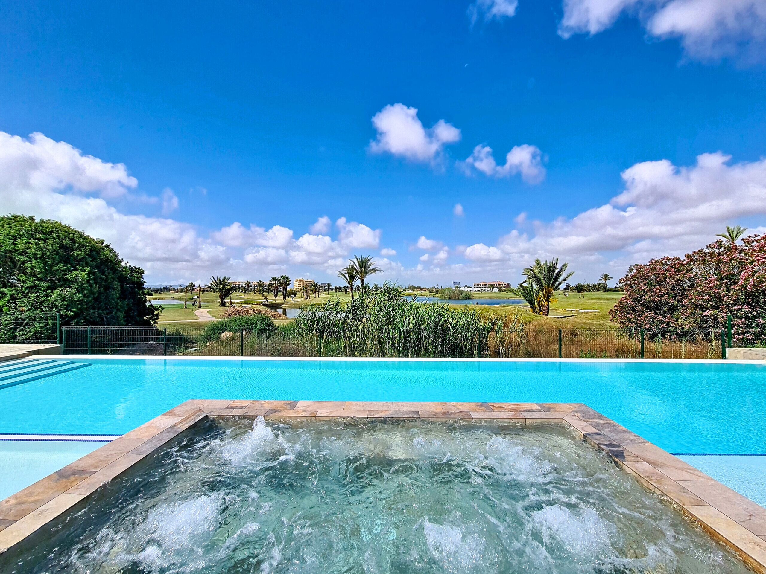 Una piscina con un jacuzzi en primer plano y un campo de golf al fondo.
