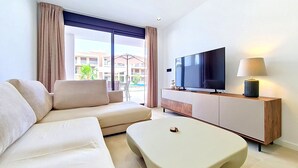 Ett modernt hotellrum med en soffa, en platt-TV, en lampa och utsikt över utomhuspoolområdet.