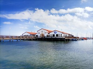 A waterfront building with a red roof, a pier extending into the water, and several boats docked nearby. - Ground Floor Oasis at La Serena Golf (Los Alcazares)