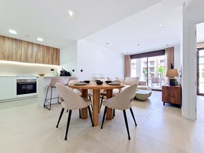 Un espace repas moderne avec une table ronde et quatre chaises, une cuisine dotée d’un four encastré et une vue sur l’extérieur grâce à de grandes fenêtres.
