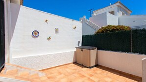 Une terrasse ensoleillée avec un sol carrelé, une petite poubelle et des éléments décoratifs sur les murs.