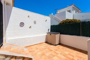 Eine sonnendurchflutete Terrasse mit Fliesenboden, einem kleinen Mülleimer und dekorativer Wandgestaltung.