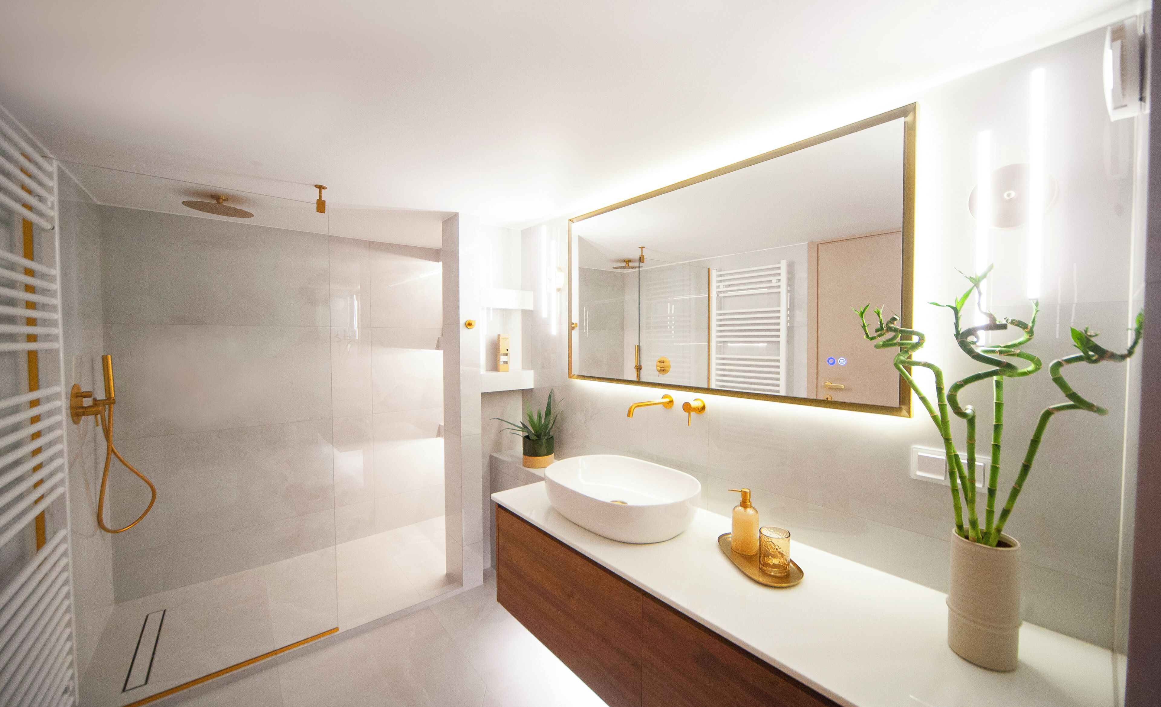 Un baño moderno con cabina de ducha de vidrio, un lavamanos blanco con detalles dorados y un espejo grande.
