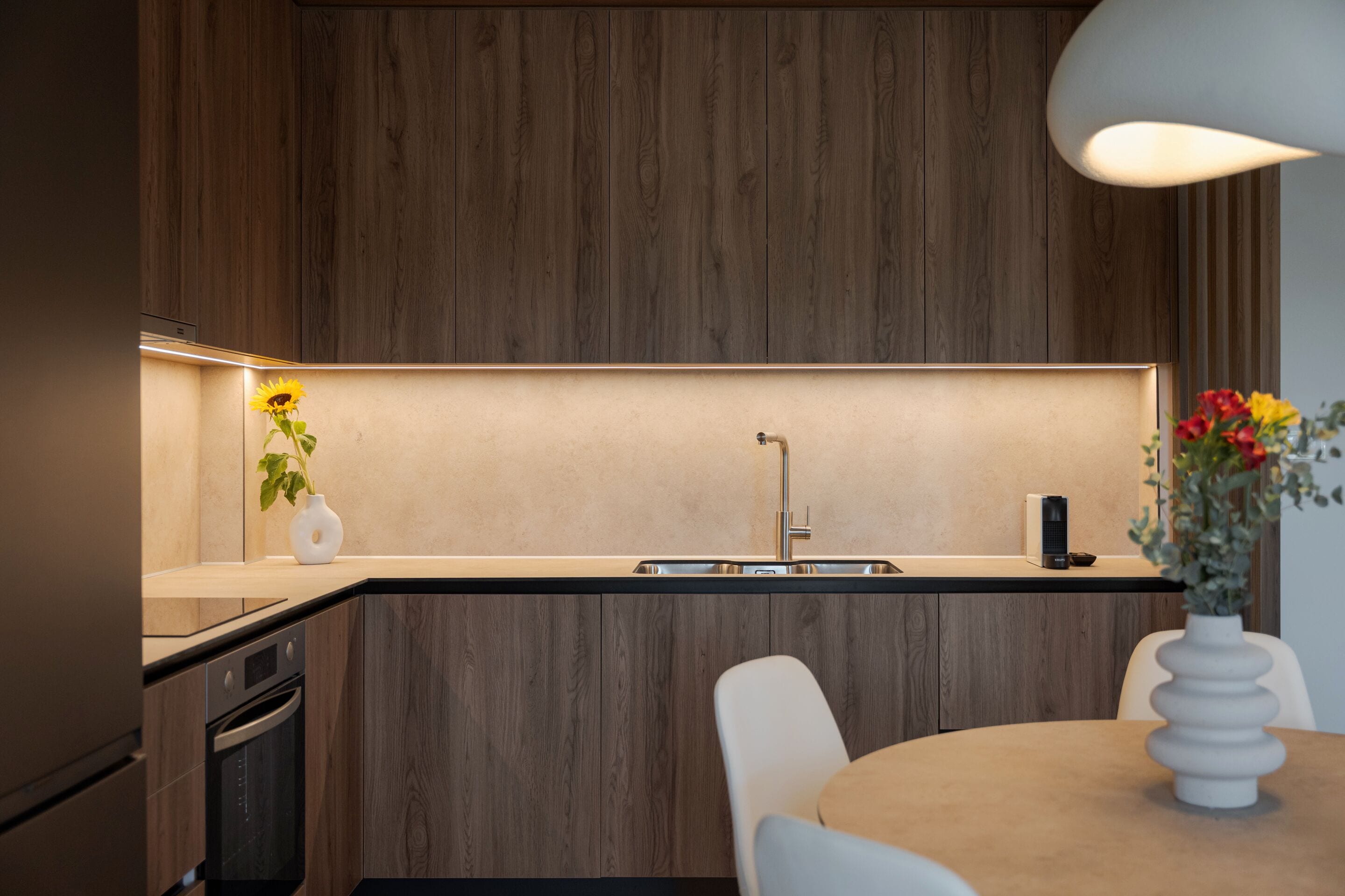 Eine moderne Küche mit Holzbeschichtung, einem Einbauofen, einer Spüle und einem Essbereich mit Tisch und Stühlen.