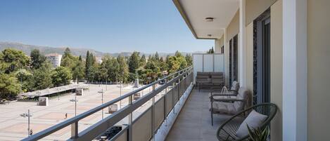 Un balcón con mobiliario exterior, vista a un paisaje urbano y cielo despejado.