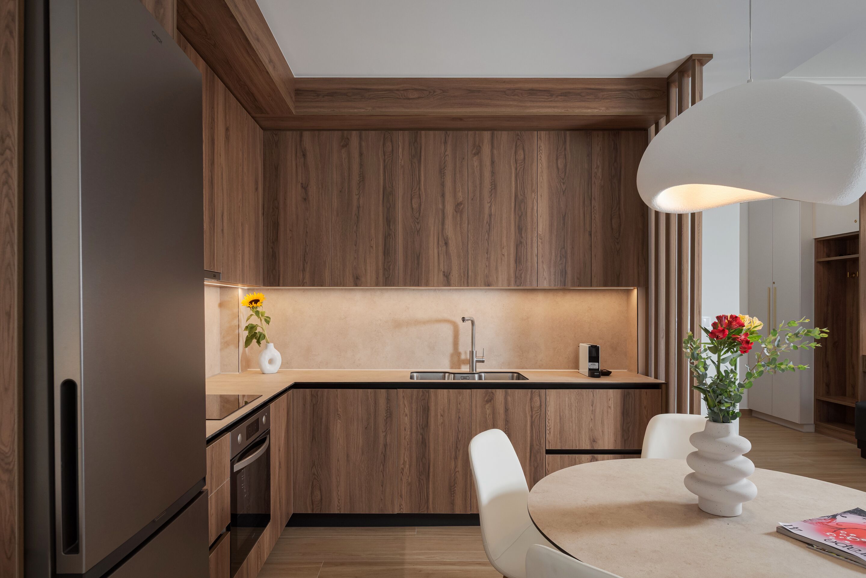 Cocina moderna con armarios de madera, horno empotrado, lavaplatos y comedor con mesa y sillas.