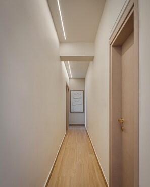 A narrow hallway with wooden flooring, a door on the right, and a framed artwork on the wall.