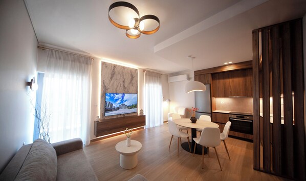 Un salon moderne comprenant un coin repas, un téléviseur fixé au mur et une cuisine avec des meubles en bois.
