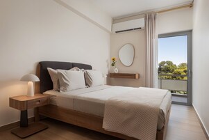 Un dormitorio con cama, mesita de noche, lámpara y vistas al verdor por una ventana.