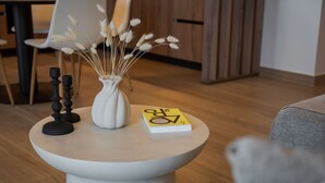 Una mesa redonda con un jarrón blanco lleno de flores secas, un candelabro negro y un libro.