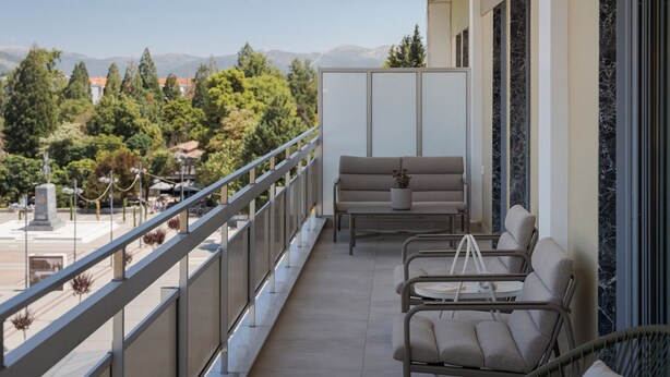 Un balcón con sofá y sillones, barandilla y vistas a árboles y montañas.
