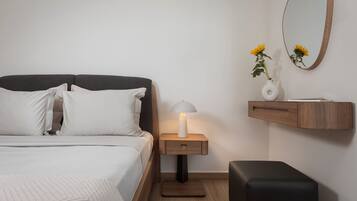 Un dormitorio ordenado con cama, mesita de noche con lámpara, un pequeño banco de madera y estante en la pared con un florero.