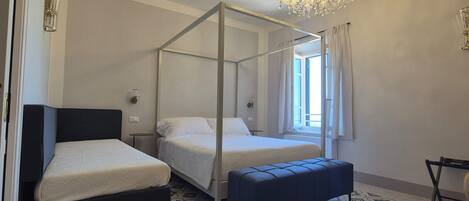 A bedroom with two beds, a canopy bed, a bench, a chandelier, and patterned floor tiles.