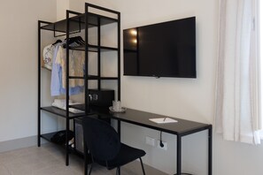 A modern room with a black desk, a black chair, a TV mounted on the wall, and a clothing rack with folded clothes.