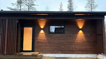 Un bâtiment en bois avec une porte noire et deux appliques murales illuminées.