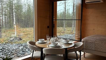 En modern inredning med ett matområde, en säng och ett stort fönster med utsikt över skogen.