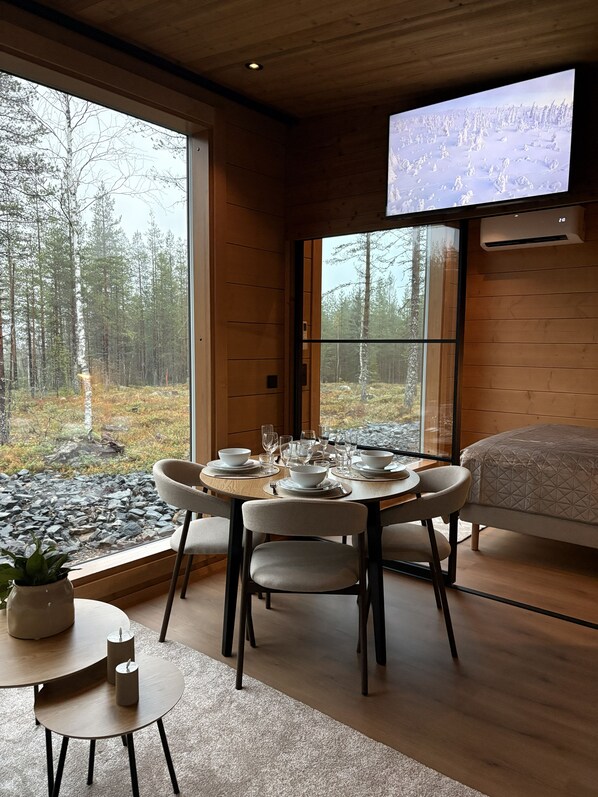 A modern interior with a dining area, a bed, and a large window offering a forest view.