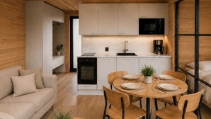 A modern interior with a wooden ceiling, a kitchen with white cabinets, a dining area with a round table and chairs, and a sofa. - Arctic Forest Suite with Private Sauna (Rovaniemi)