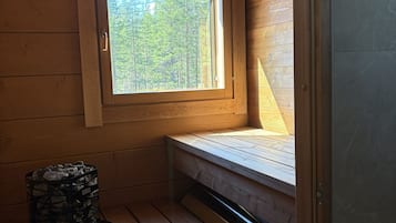 L’intérieur d’un chalet en bois, avec un plafond en pente, une fenêtre donnant sur les arbres, un banc intégré et une cheminée en pierre.