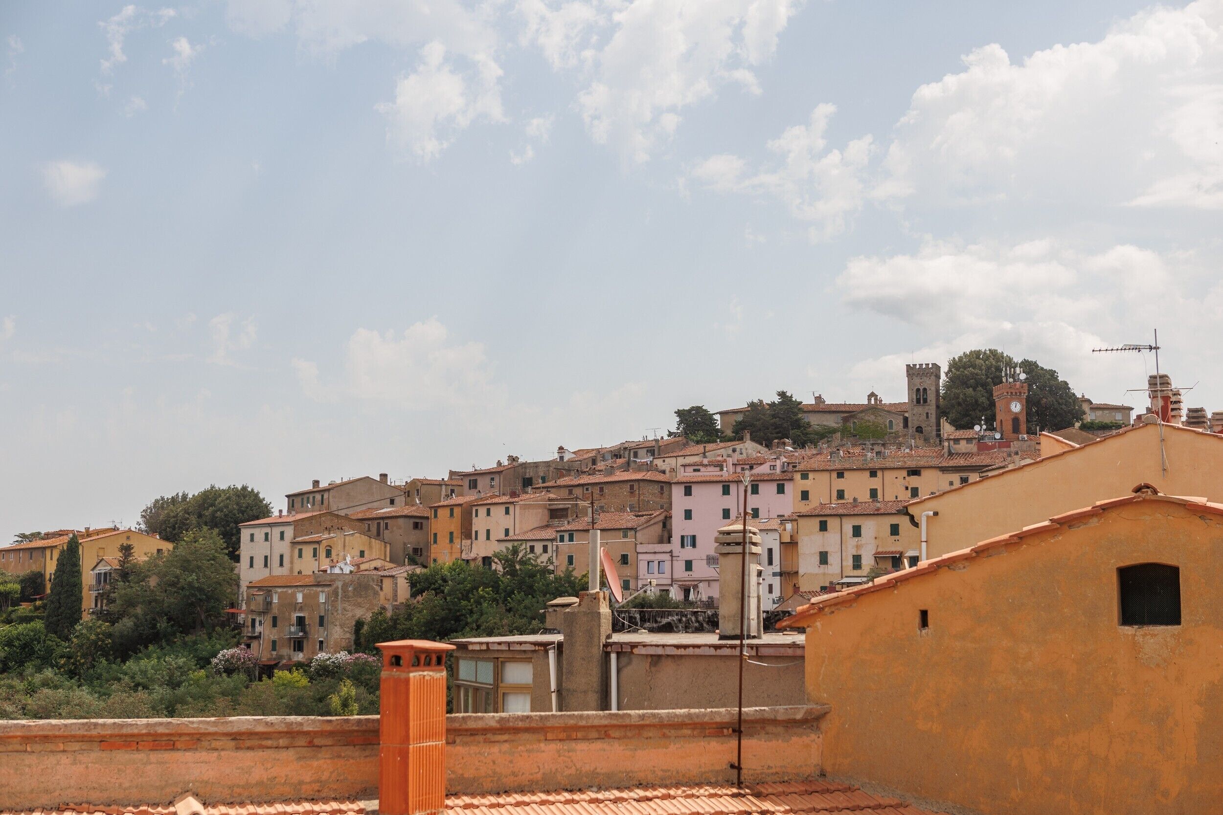 Vista de uma cidade com edifícios de telhado em terracota, uma torre do relógio imponente e um céu claro.