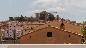 A balcony with a white chair, overlooking a historic town with terracotta-roofed buildings and a prominent tower. - Il Vicolo Spacious Room in the Village – Experience Village Charm with Style (Castagneto Carducci)