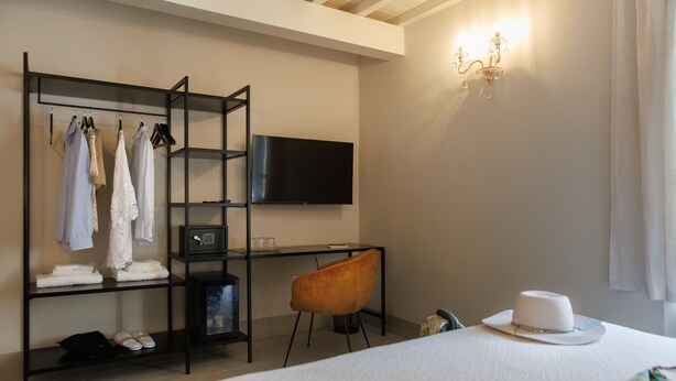 A hotel room with a bed, a desk with a television, a wardrobe, and a chair. - Il Vicolo Spacious Room in the Village – Experience Village Charm with Style (Castagneto Carducci)