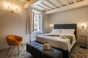 A hotel room with a bed, a chair, a bedside table, and a window with curtains.