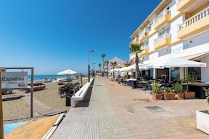 A beachside walkway with outdoor seating, palm trees, and a sign for Karabas Beach. - Ocean Views on the Sabinillas Boardwalk (San Luis de Sabinillas)