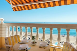 A balcony with a table set for dining, overlooking a beach with umbrellas and people. - Ocean Views on the Sabinillas Boardwalk (San Luis de Sabinillas)