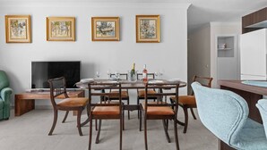 A dining area with a round table, six chairs, a flat-screen TV, and framed artwork on the wall. - Ocean Views on the Sabinillas Boardwalk (San Luis de Sabinillas)