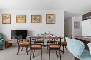 A dining area with a round table, six chairs, a flat-screen TV, and framed artwork on the wall. - Ocean Views on the Sabinillas Boardwalk (San Luis de Sabinillas)