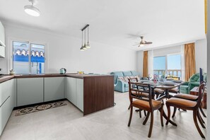 A modern kitchen with a central island, dining area with wooden chairs, and a view of the sea through large windows. - Ocean Views on the Sabinillas Boardwalk (San Luis de Sabinillas)