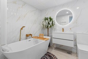 Une salle de bain moderne avec une baignoire sur pieds, une chaise en bois, un miroir rond et un meuble-lavabo blanc.