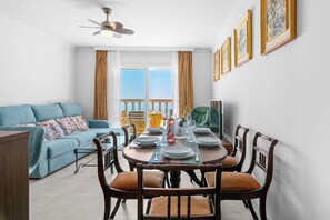 A dining area with a table set for four, a blue sofa, and a balcony with a view. - Ocean Views on the Sabinillas Boardwalk (San Luis de Sabinillas)