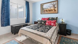 A bedroom with a bed, curtains, a painting, and a nightstand. - Ocean Views on the Sabinillas Boardwalk (San Luis de Sabinillas)