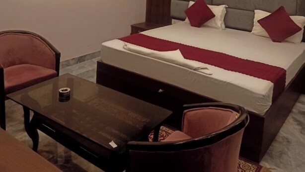 Una camera d'albergo con un letto, due poltrone, un tavolino, una ventola a soffitto e un condizionatore d'aria.