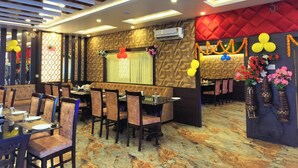 Un ristorante con interni moderni, che presenta un lungo tavolo da pranzo con sedie, un muro decorato con motivi e elementi decorativi come palloncini e fiori.