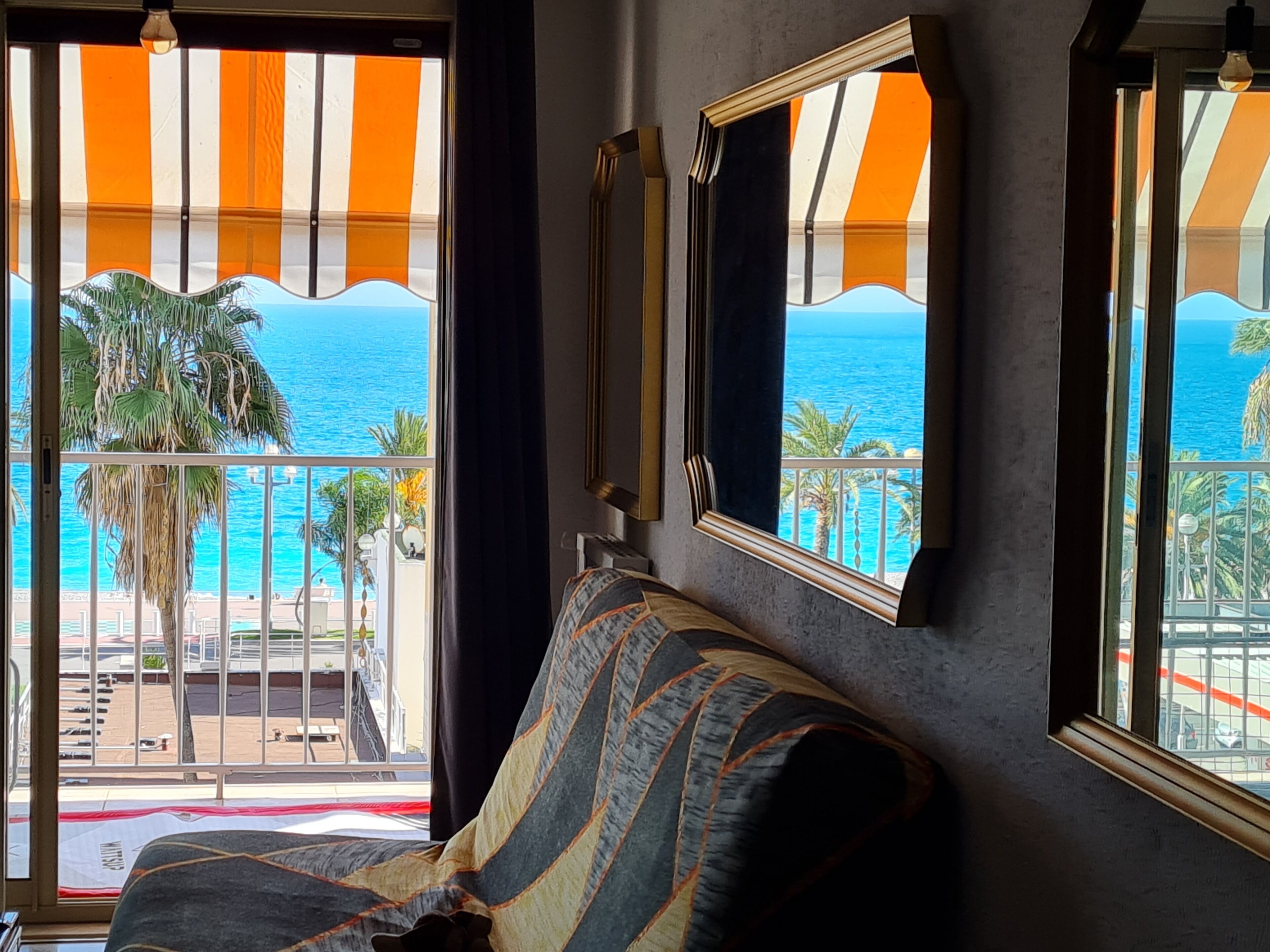 Habitación con vista al mar a través de amplios ventanales, un sofá y un espejo en la pared.