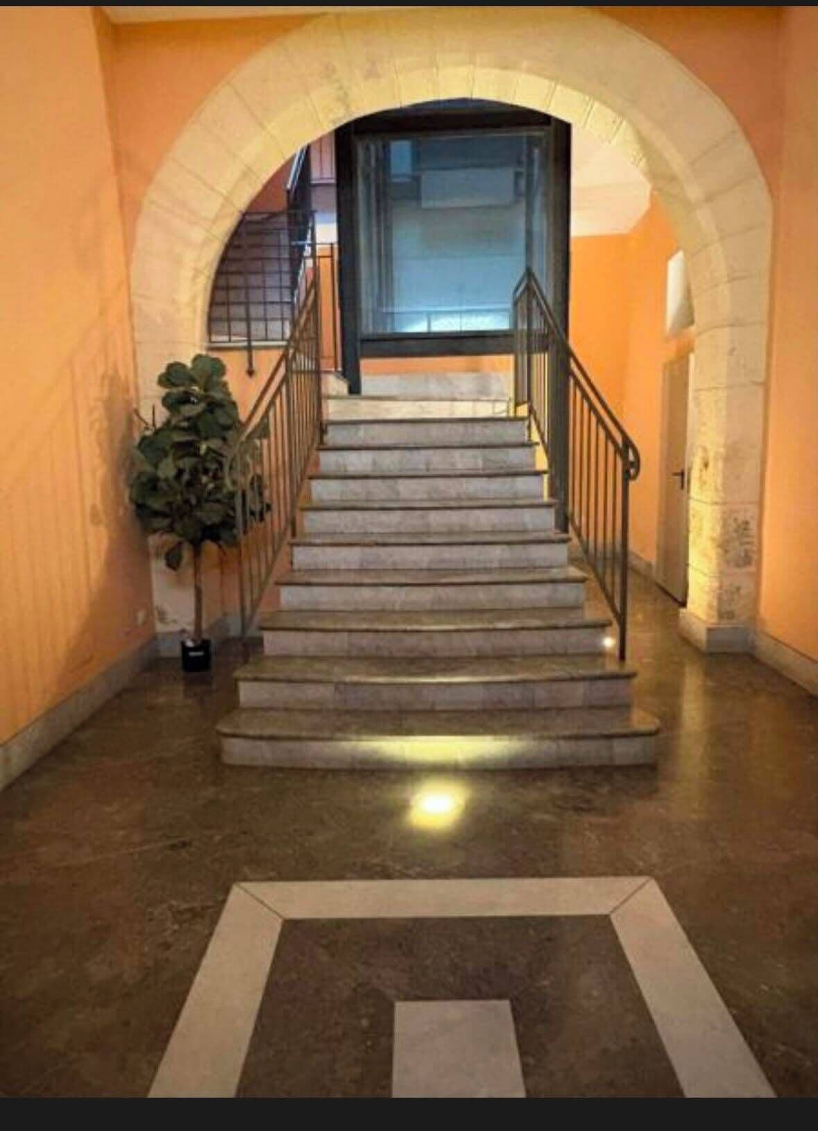 A staircase with a stone balustrade leading to a door, surrounded by walls and a potted plant.