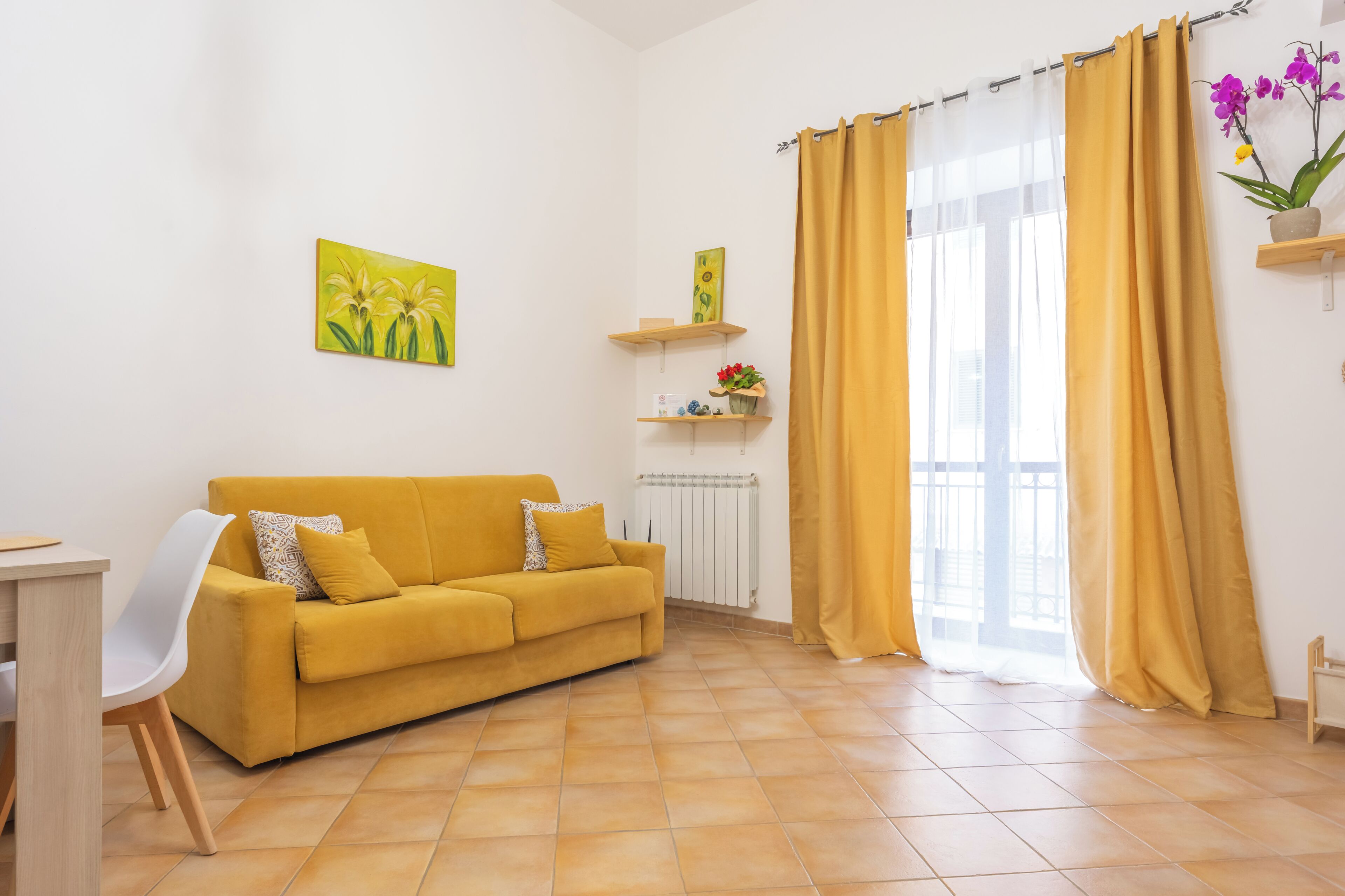 Una sala de estar con un sofá amarillo, una silla blanca, un radiador y una ventana con cortinas amarillas.