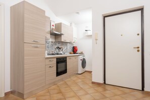 Eine kleine Küche mit Herd, Backofen und Waschmaschine, Holzschränken und Fliesenboden.