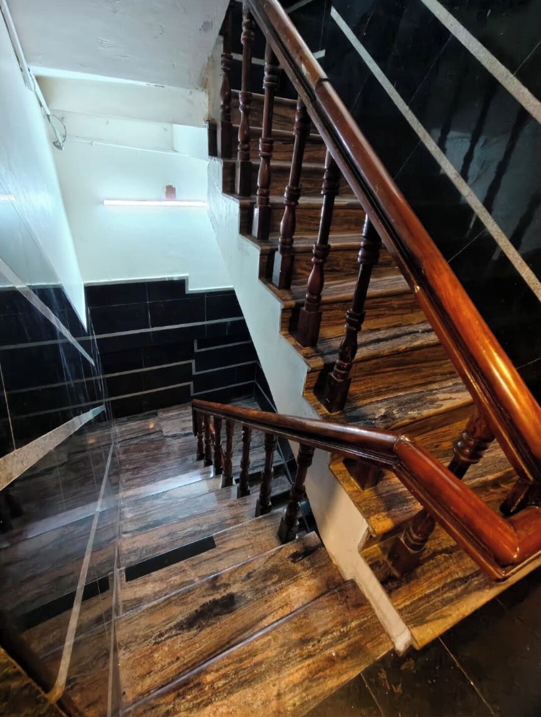 A staircase with wooden balusters and a handrail, leading to a landing with black and white tiled walls.