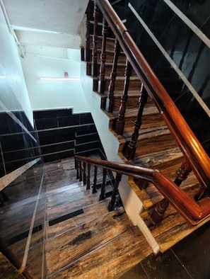 A staircase with wooden balusters and a handrail, leading to a landing with black and white tiled walls.
