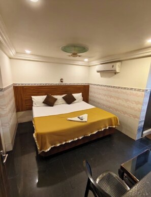 A hotel room with a bed, a bedside table, a chair, and an air conditioning unit. - HOTEL SVR  ELITE (Vijayawada)