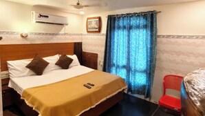 Habitación de hotel con cama, escritorio, silla, unidad de aire acondicionado y ventana con cortinas.