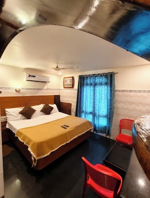 Habitación de hotel con cama, escritorio, silla, unidad de aire acondicionado y ventana con cortinas.
